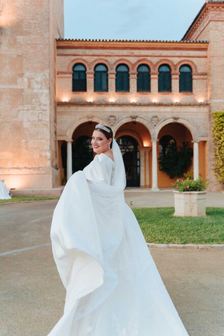 Bride smiling and holding her dress in front of Castillo de la Monclova during a wedding in Seville.