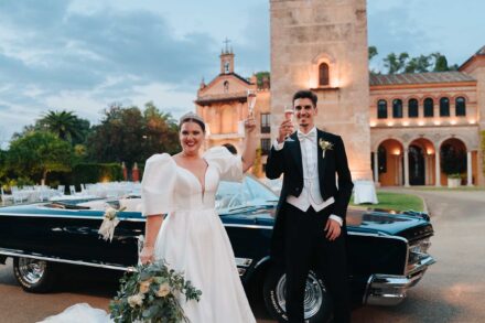 Bride and groom toasting with champagne beside a vintage car at Castillo de la Monclova in Seville