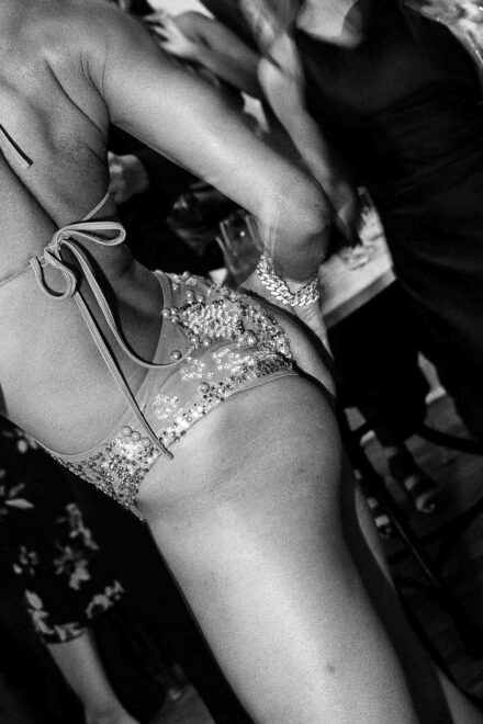 Una artista de espaldas con body de pedrería y pulsera brillante, la mano en la cadera, en blanco y negro