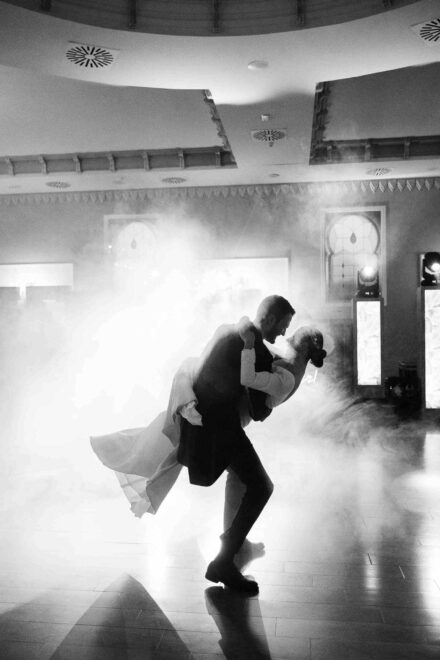 El novio inclina a la novia hacia atrás en pleno baile, a contraluz y entre humo, en blanco y negro