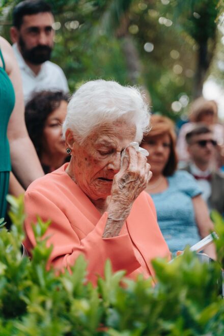 Una invitada mayor de pelo blanco y chaqueta coral se enjuga los ojos con un pañuelo durante la ceremonia