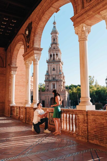 Un chico pide matrimonio de rodillas a su pareja bajo los arcos de la plaza de España de Sevilla, con la torre al fondo