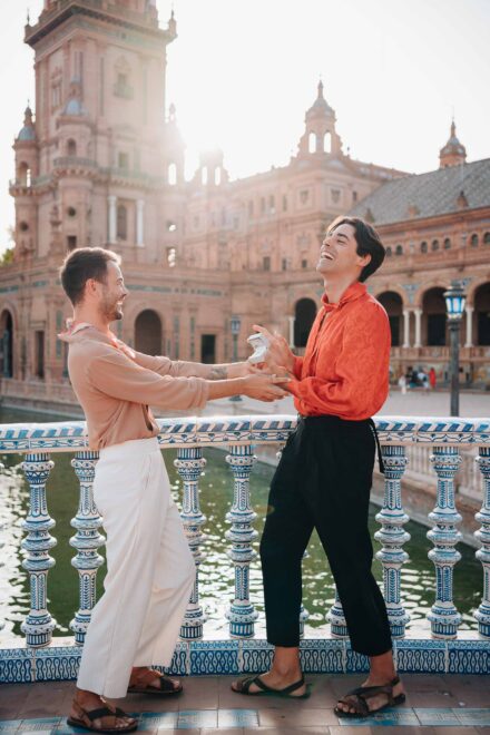 Dos chicos ríen mientras uno ofrece un anillo al otro sobre el canal de la plaza de España de Sevilla