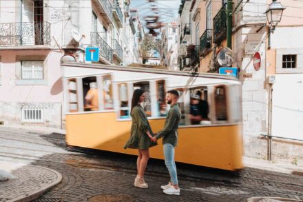 La pareja, de la mano, se mira mientras un tranvía amarillo pasa movido detrás de ellos