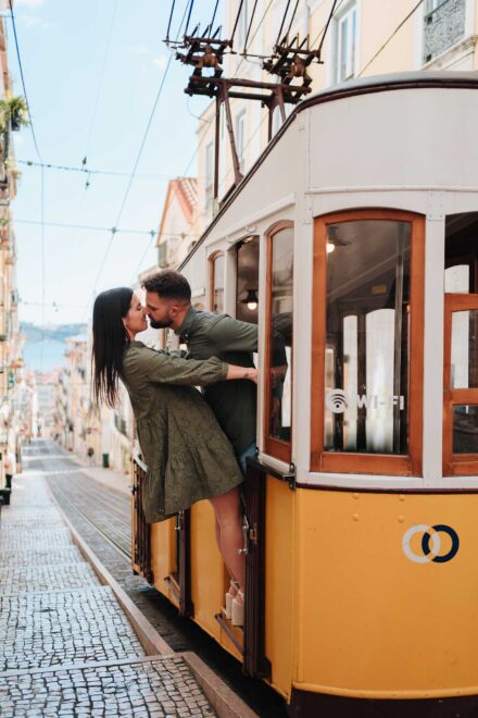 La pareja se besa asomada a la puerta de un funicular amarillo en una calle empinada de Lisboa