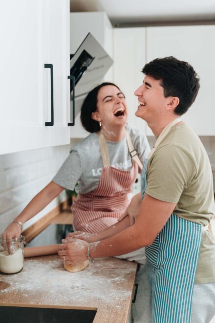 La pareja se ríe a carcajadas en la cocina, con delantales de rayas, mientras amasa en la encimera enharinada