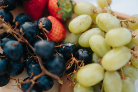 Un anillo de compromiso con diamante apoyado entre uvas negras, uvas blancas y fresas