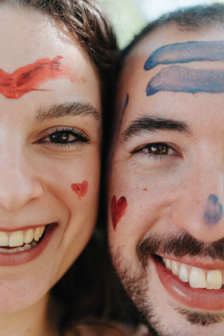 Primer plano de las caras de la pareja, mejilla con mejilla, pintadas con corazones y trazos de colores