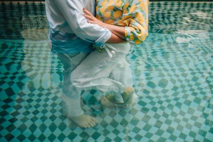 Los novios se abrazan de pie dentro de la piscina, con la ropa mojada, vistos del pecho a los pies