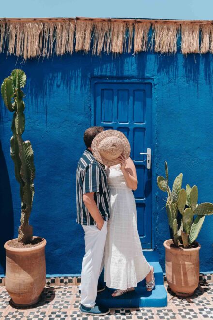 La novia tapa el beso con su sombrero de paja ante una puerta azul flanqueada por dos cactus