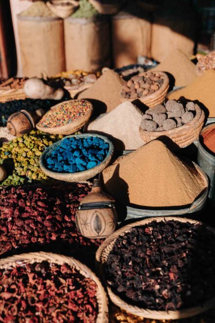 Especias en polvo amontonadas y cestos de flores secas y piedras azules en un puesto del mercado