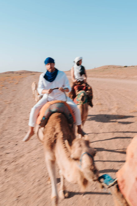 El novio, con turbante azul, avanza en camello por el desierto seguido de la novia