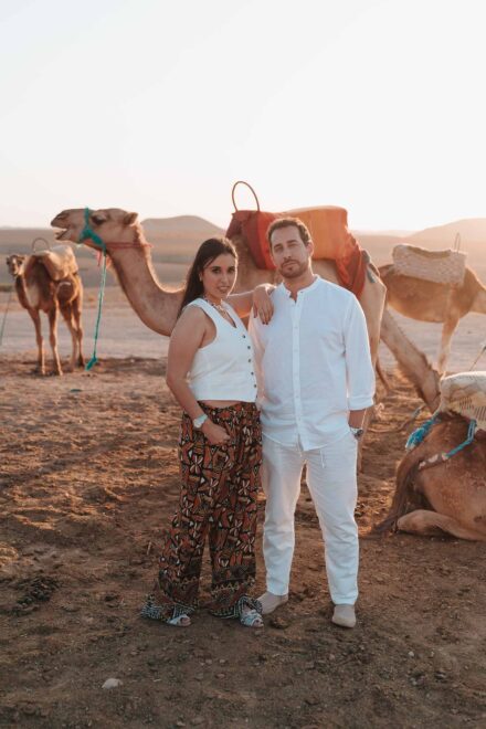 La pareja posa en el desierto con luz dorada, delante de varios camellos ensillados