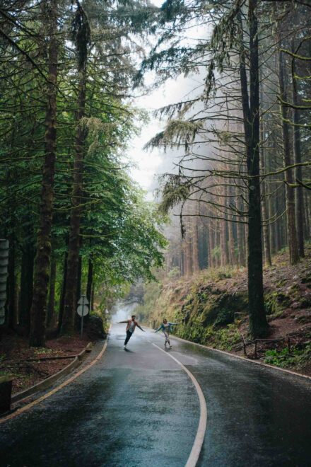 La pareja baila con los brazos abiertos en una carretera mojada entre árboles altos y niebla
