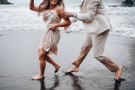 La novia se recoge el vestido y ríe mientras el novio la persigue descalzo por la orilla