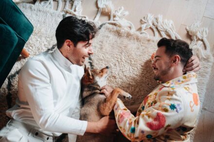 Los novios se ríen tumbados en una alfombra de flecos con un perro entre los dos