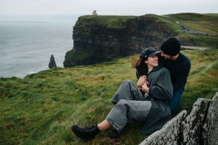 La pareja se abraza sentada en la hierba durante su preboda en los acantilados de Moher (Irlanda)