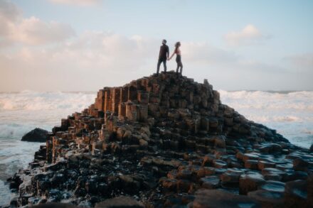 Los novios de la mano en lo alto de las columnas de basalto de la Calzada del Gigante, con el mar embravecido
