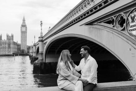 Los novios, sentados a orillas del Támesis, se sonríen junto al puente de Westminster, en blanco y negro