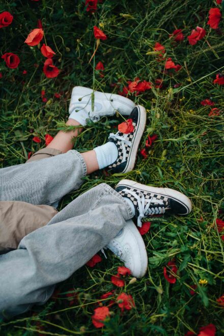 Pies de las novias con zapatillas blancas y de cuadros en blanco y negro, tumbadas entre amapolas