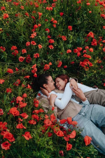 Las novias tumbadas y abrazadas en un campo de amapolas, riéndose frente a frente