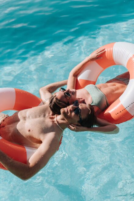 Los novios flotan en la piscina sobre flotadores naranjas y blancos, cabeza con cabeza y con gafas de sol