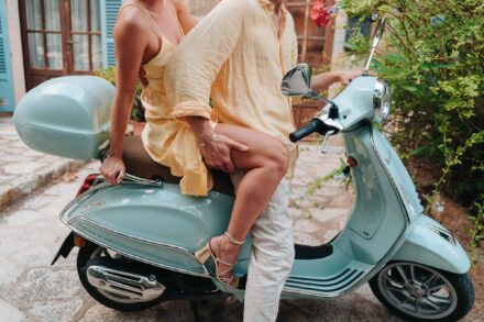Detalle de los novios, vestidos de amarillo claro, sentados en una moto azul claro en una calle empedrada
