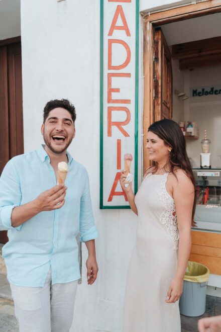 Los novios se ríen con un cucurucho de helado cada uno junto al cartel vertical de una heladería