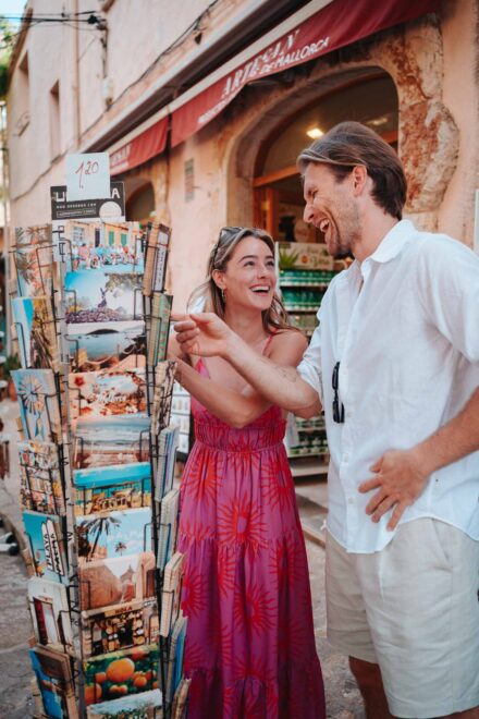 La novia y el novio se ríen a carcajadas junto a un expositor de postales a la puerta de una tienda