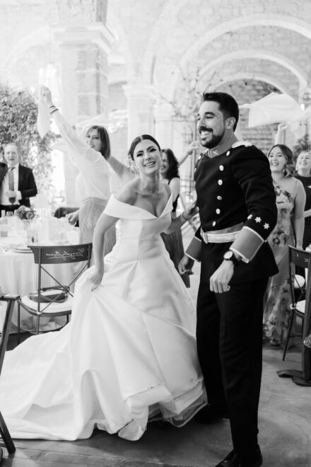 Los novios, él con uniforme militar de gala, entran bailando al banquete entre servilletas al aire, en blanco y negro