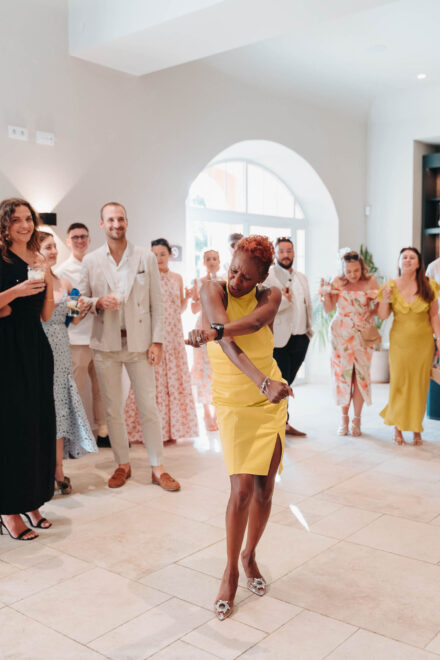 Una invitada con vestido amarillo y pelo corto cobrizo baila en el centro mientras los demás la miran sonrientes