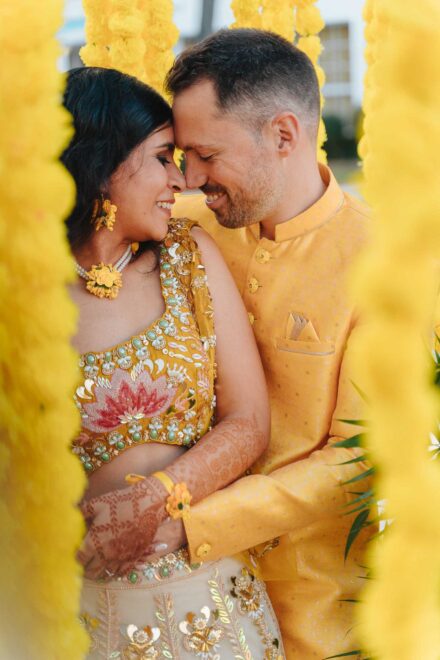 Los novios, vestidos de amarillo, juntan las frentes sonriendo entre guirnaldas de flores amarillas