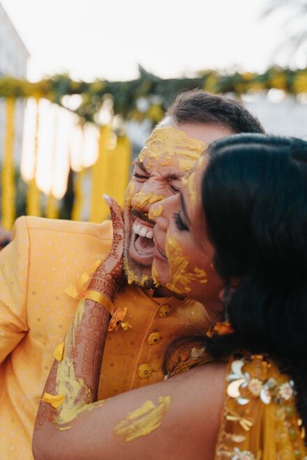 Los novios se ríen mejilla con mejilla, con la cara untada de pasta amarilla durante el haldi