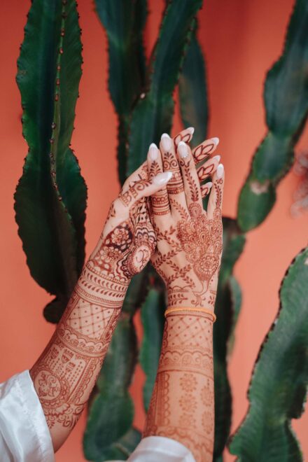 Las manos de la novia, cubiertas de henna, levantadas frente a un cactus y una pared terracota