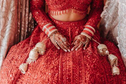 Las manos de la novia, con henna, pulseras rojas y kalire, descansan sobre su falda roja de lentejuelas