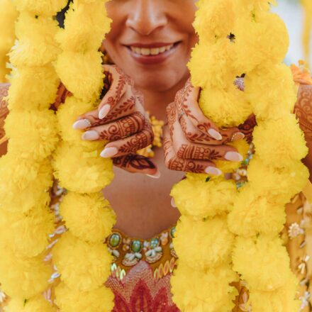 La novia sonríe con las manos cubiertas de henna, sujetando dos guirnaldas de flores amarillas