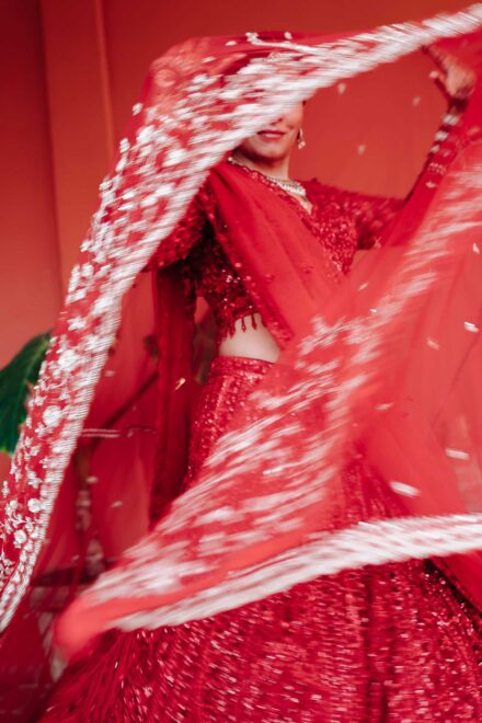 La novia, con lehenga roja de lentejuelas, hace girar su velo bordado, que le tapa media cara