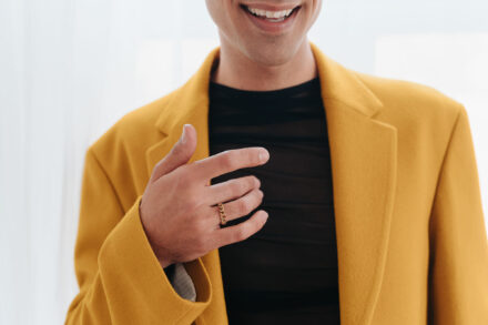 Detalle de la mano de uno de los novios, con un anillo dorado de eslabones, sobre su americana mostaza