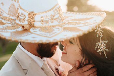 Los novios, a punto de besarse, bajo un sombrero de charro blanco y dorado; ella lleva un tocado de pedrería