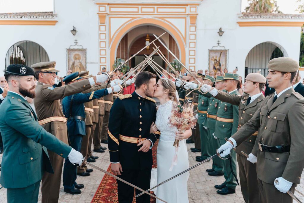 Smiling bride and groom exiting the church under an arch of swords held by uniformed soldiers during a military wedding in Seville