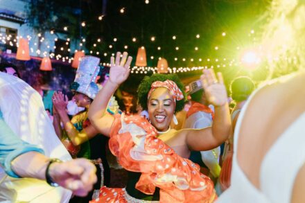 Una bailarina con traje de volantes naranjas y pañuelo de lunares baila con los brazos en alto bajo guirnaldas de luces