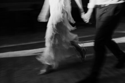 Los novios caminan de la mano, movidos por la velocidad, con los flecos del vestido al vuelo entre franjas de luz