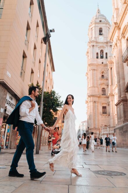Los novios caminan de la mano, ella con vestido de flecos, con la torre de la catedral de Málaga al fondo