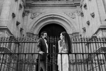 Los novios se miran apoyados en una reja de hierro frente a una gran portada de piedra