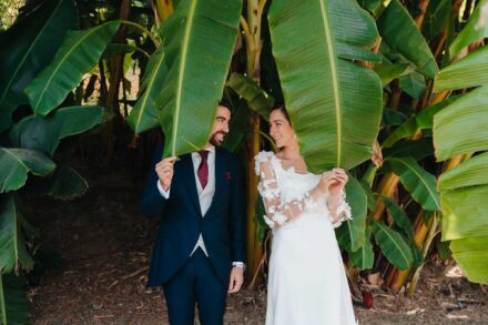 Los novios asoman bajo unas hojas de platanera y se miran sonriendo