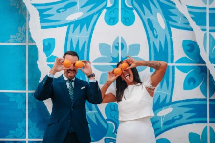 Los novios se tapan los ojos con naranjas y sacan la lengua delante de un mural azul con motivos de azulejo