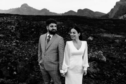 Los novios de la mano en un campo de lava, ella sonriéndole y él mirando a un lado, en blanco y negro