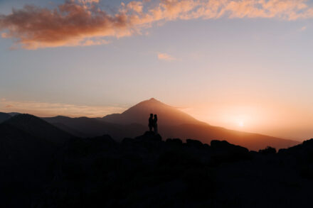 Los novios, en silueta sobre unas rocas, con el Teide y el sol bajo en el horizonte