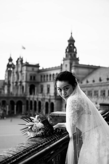 La novia, con velo y ramo, mira atrás apoyada en la barandilla de la plaza de España de Sevilla, en blanco y negro