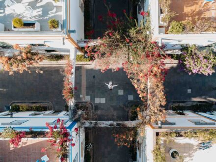 Los novios en un cruce de calles blancas bajo arcos cubiertos de buganvillas, vistos desde el aire
